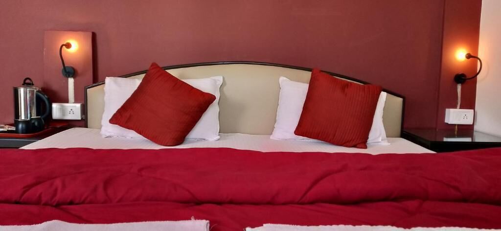Ein ordentlich bezogenes Bett mit roter und weißer Bettwäsche, zwei Nachttischlampen und eine Kaffeemaschine auf dem Nachttisch.