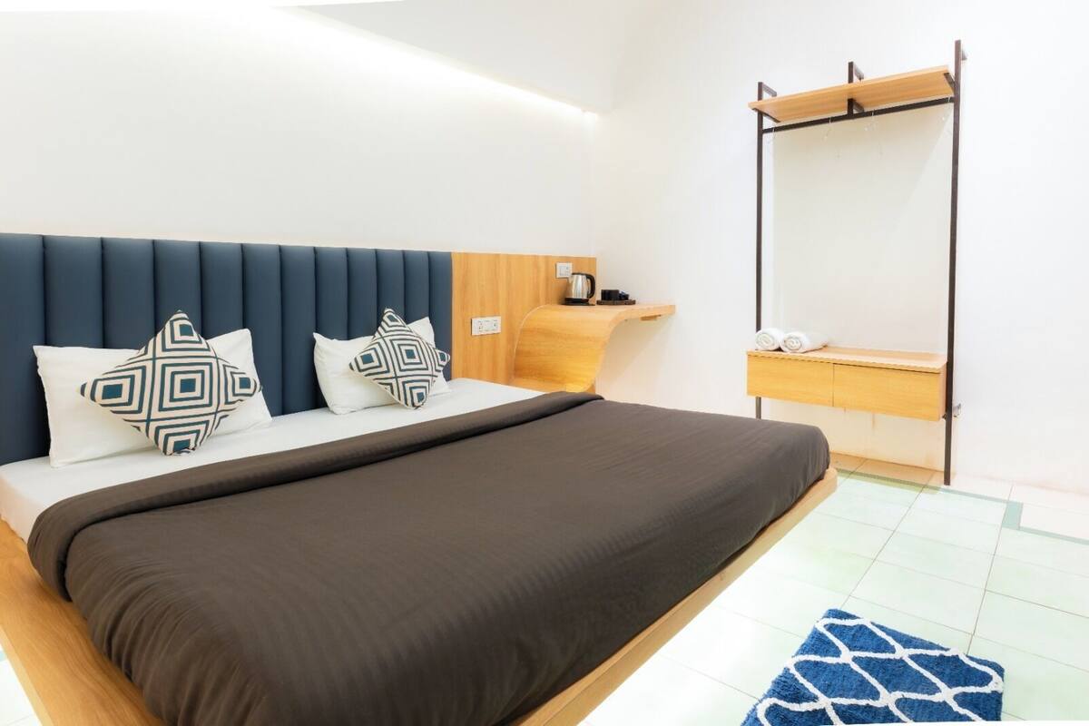 A modern hotel room with a bed, a wooden nightstand, a mirror, and a blue patterned rug.