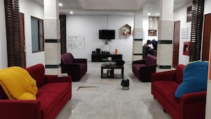 A living room with red sofas, a coffee table, a TV, and a fireplace. - Joey's Hostel Agra (Agra)