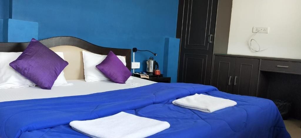 Une chambre d’hôtel comprenant un lit, deux oreillers, une table de chevet, une bouilloire et une armoire.