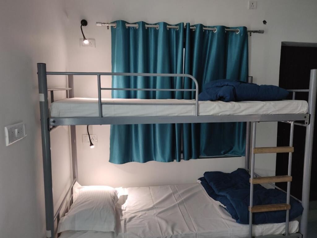 Dormitorio con literas, una escalera de metal, ropa de cama blanca y cortinas color turquesa.