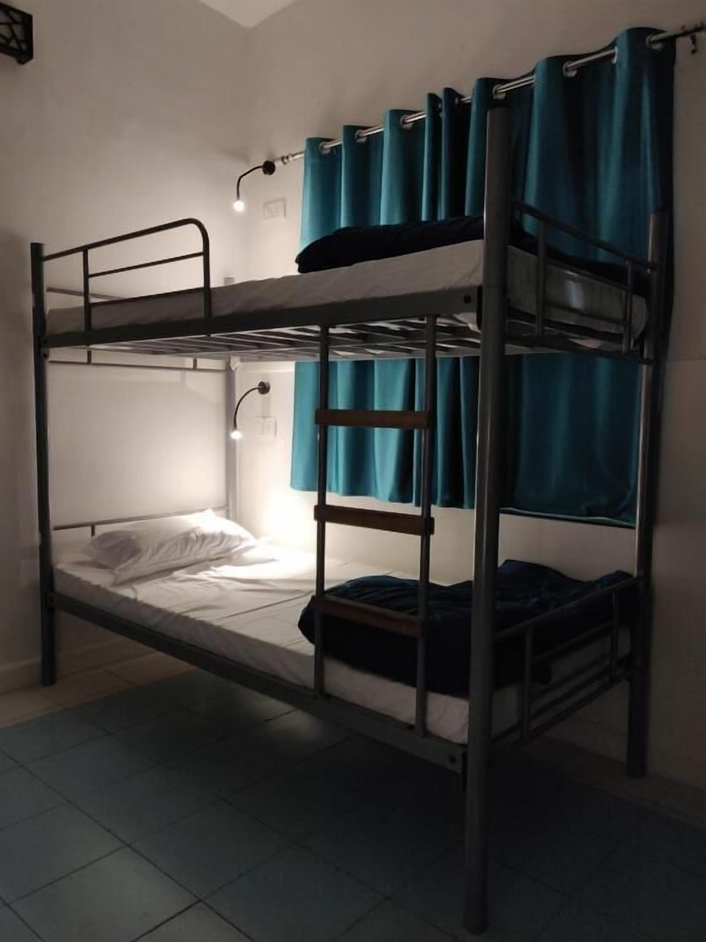 Un lit superposé avec une échelle, un lit simple en dessous et une fenêtre avec des rideaux.