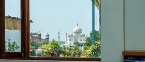 A view of the Taj Mahal through a window with potted plants in the foreground.