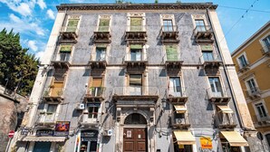 A historic building with multiple balconies, a central entrance, and various commercial establishments on the ground floor. - Quiet and cozy in the center, one step away from everything and with a unique view (Catania)
