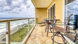 Un balcon avec une table et des chaises, donnant sur une plage et une zone herbeuse.