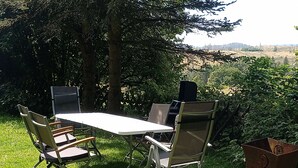 An outdoor dining area with a table and chairs, surrounded by greenery and trees.