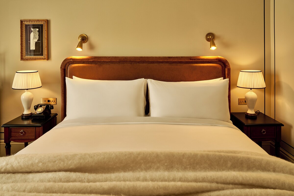 A neatly made bed with a wooden headboard, two bedside tables with lamps, and a framed picture on the wall.