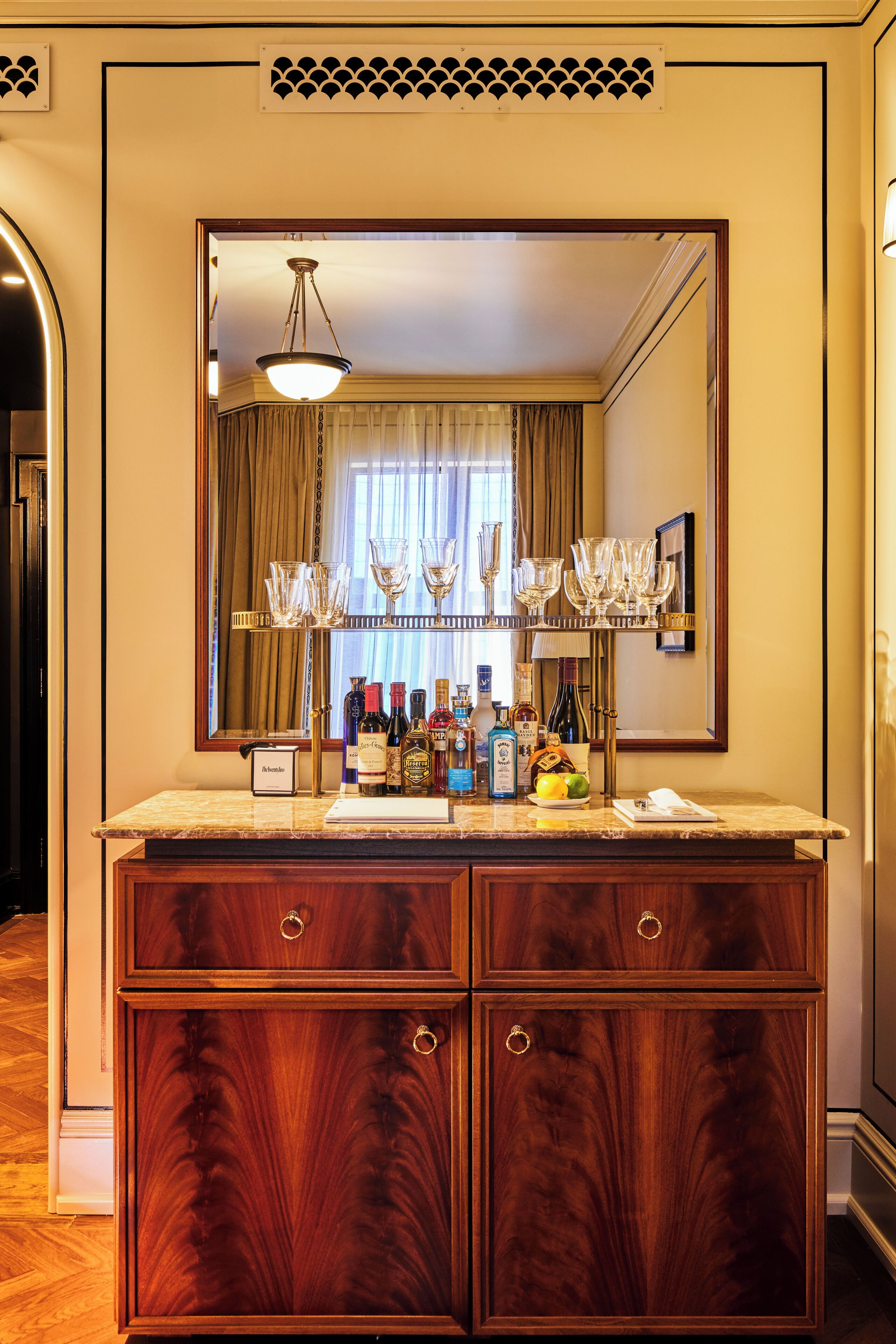 A bar area with a wooden cabinet, a mirror, and a shelf with glasses and bottles.