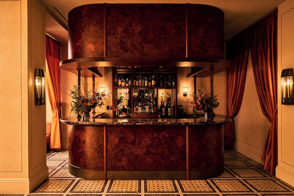 A bar area with a circular marble counter, multiple bottles, and two potted plants. - The Twenty Two New York (New York)