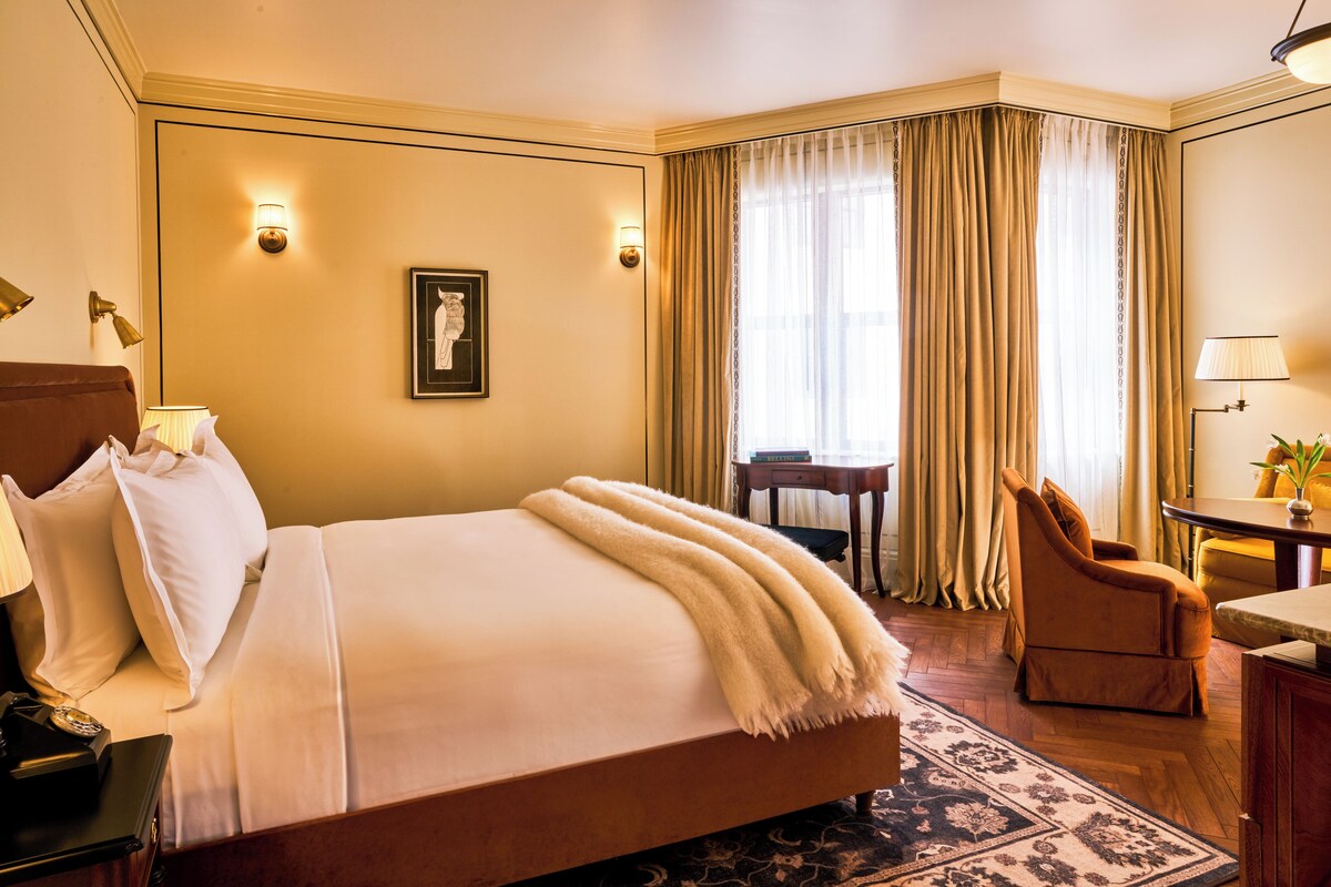 A hotel room with a large bed, a desk, a chair, and a window with curtains.