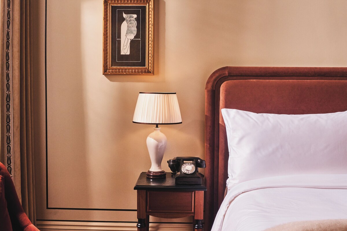 A hotel room with a bed, a chair, a nightstand with a lamp, and a framed picture on the wall.
