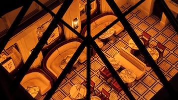 Een interieur met hoge plafonds en een geometrisch patroon, met meerdere zithoeken en een centraal, rond gebied, gezien door een geometrisch raam.