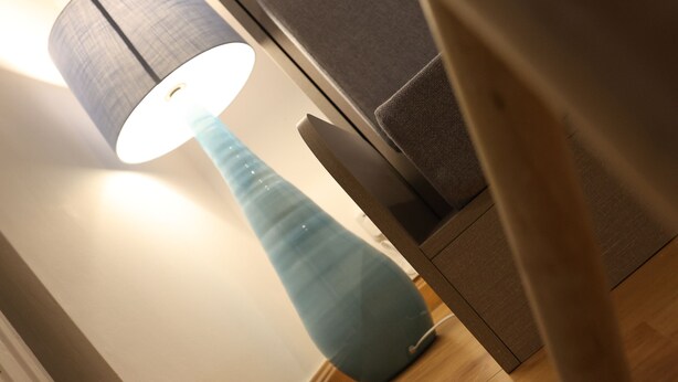 Ein Zimmer mit Holzboden, einer hohen, blauen Lampe und einem Sessel.