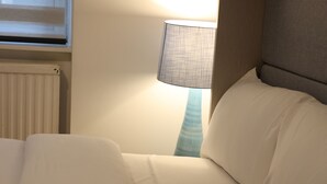 Ein ordentlich bezogenes Bett mit weißen Bettwäsche, eine Nachttischlampe und ein Fenster mit Jalousien.
