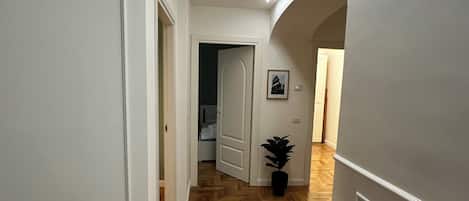A hallway with wooden flooring, white walls, and an arched doorway leading to another room.