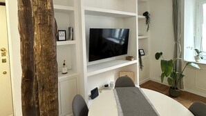 A modern living room with a large flat-screen TV, white shelving, a dining table with chairs, and a potted plant. - Apartment in elegant Via Veneto 2 minutes from the center of Rome (Roma)