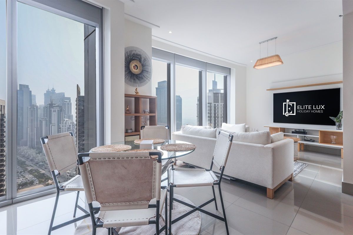 A modern living room with a large TV, a dining area with round tables, and a city view.
