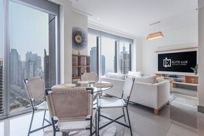 A modern living room with a large TV, a dining area with round tables, and a city view. - Exclusive 1 BHK at Opera Grand, Downtown Dubai (Dubai)