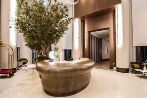 A modern lobby with a central reception desk, a large indoor plant, and a minimalist design. - Exclusive 1 BHK at Opera Grand, Downtown Dubai (Dubai)