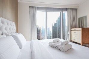 A hotel room with a large bed, a wooden dresser, and a view of tall buildings through the window. - Exclusive 1 BHK at Opera Grand, Downtown Dubai (Dubai)