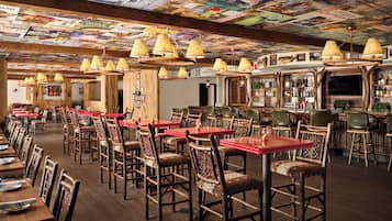A restaurant with wooden tables and chairs, a bar area, and a ceiling covered with posters.