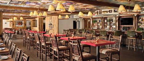 Un restaurant avec des tables et des chaises en bois, un coin bar et un plafond recouvert de posters.