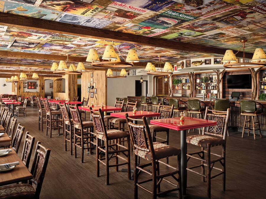 A restaurant with wooden tables and chairs, a bar area, and a ceiling covered with posters.