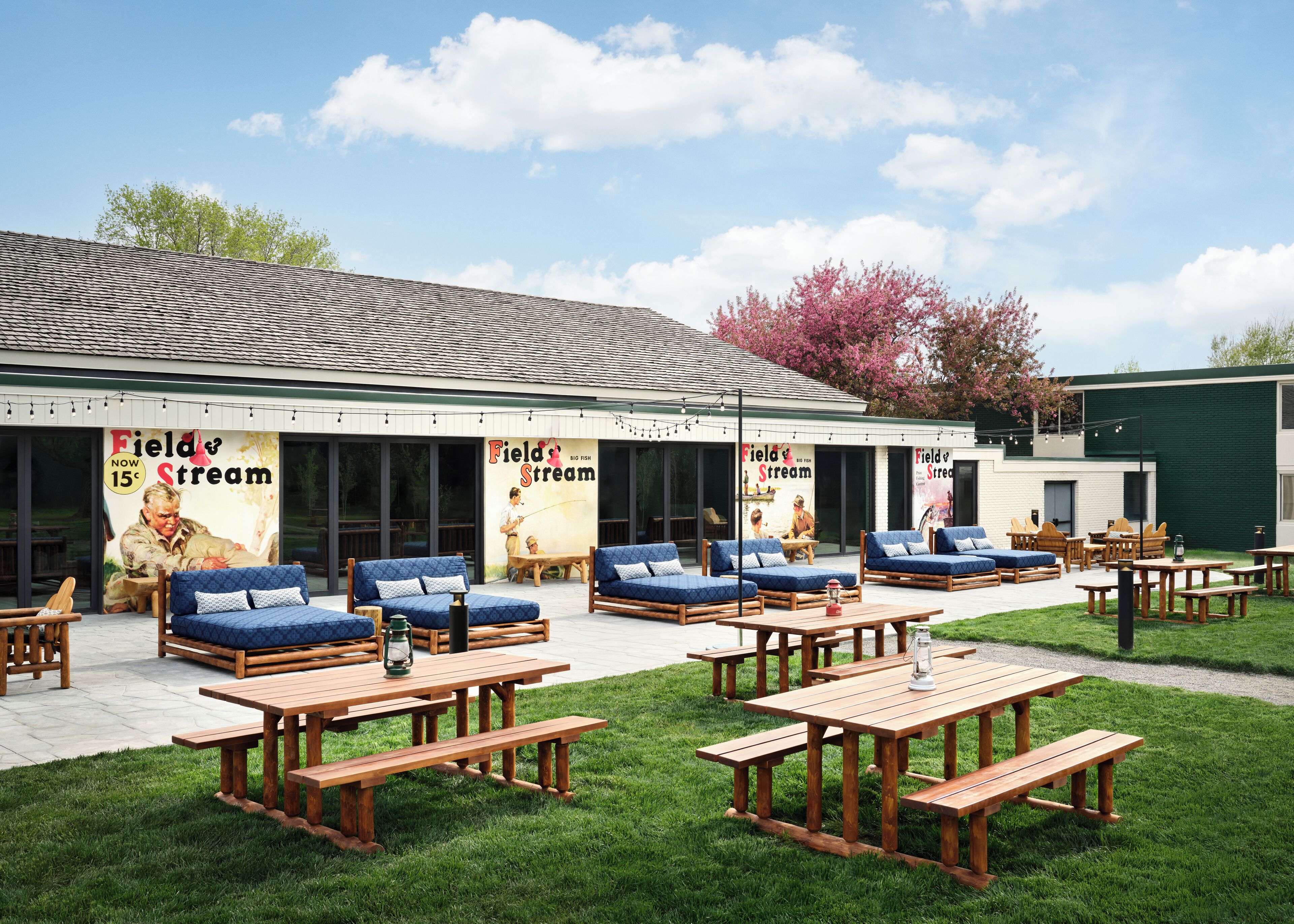 Un espacio de asientos al aire libre con bancos de madera y sofás con cojines azules, un gran cartel que anuncia 'Field & Stream', y un césped.
