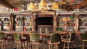 A bar area with wooden stools, a bar counter, and shelves stocked with bottles. - Field & Stream Lodge Bozeman (Bozeman)