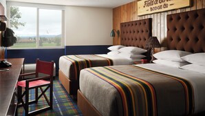 A hotel room with two beds, a desk, a chair, and a large window offering a view of the outdoors.
