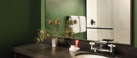 A bathroom with a green wall, a large mirror, a sink with a wooden vanity, and three blue wall-mounted lights.