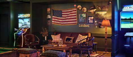 Ein gemütliches Zimmer mit Holzbalkendecke, einer großen amerikanischen Flagge, einem Billardtisch und einem Fernseher, der ein Golfspiel zeigt.