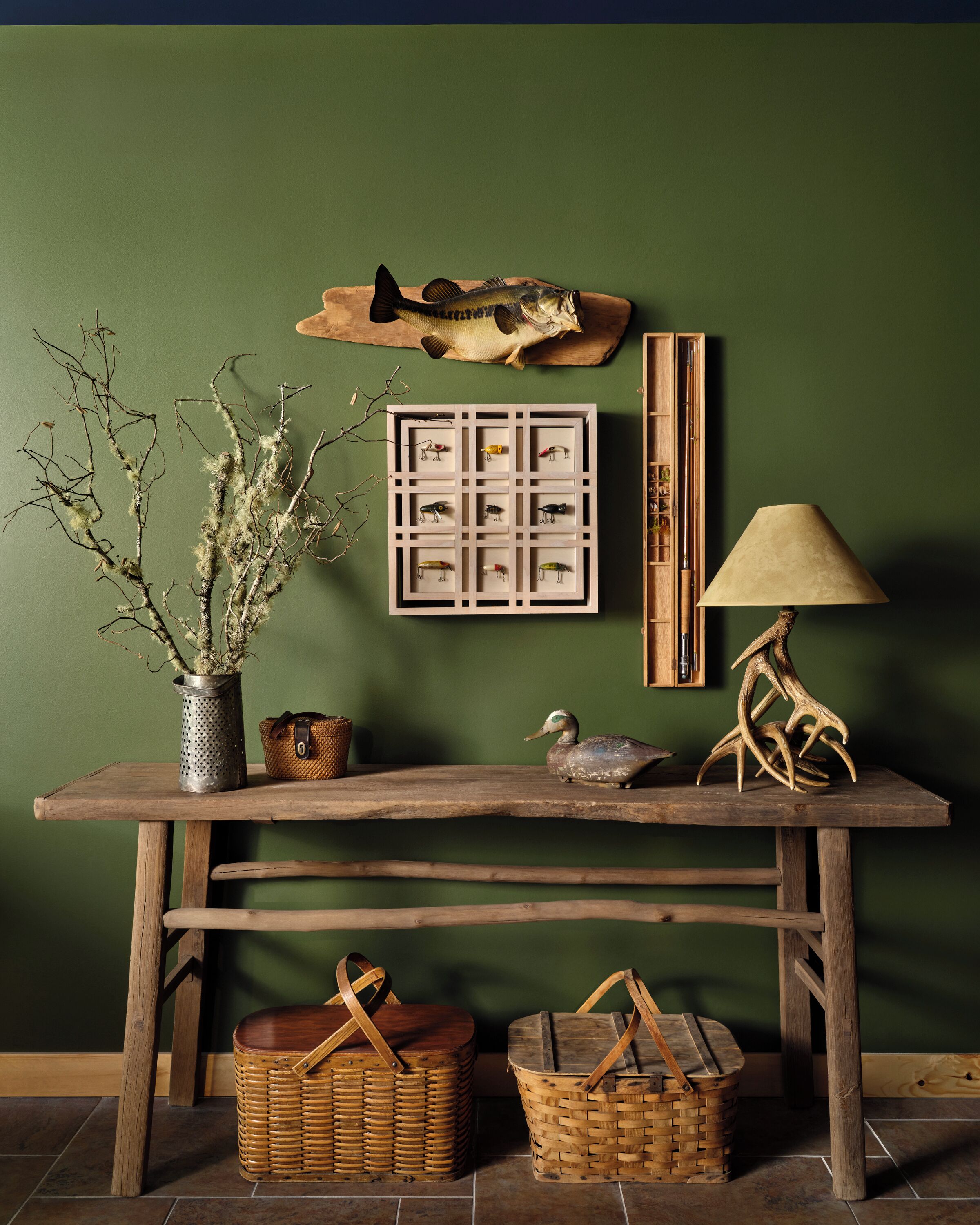 Een rustieke houten tafel met een lijst met vis, een lamp en decoratieve voorwerpen tegen een groene muur.
