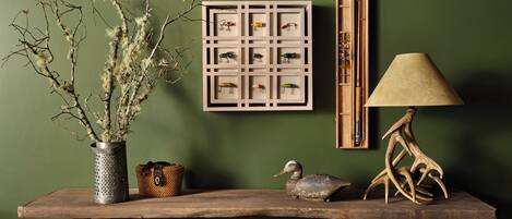 A rustic wooden table with a framed fish, a lamp, and decorative items against a green wall.