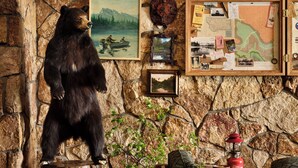 A rustic room with a bear statue, framed maps, and a wooden table with a lantern. - Field & Stream Lodge Bozeman (Bozeman)