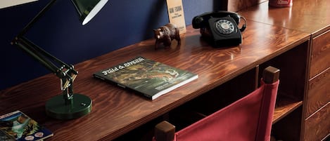 Ein Holztisch mit einer grünen Schreibtischlampe, einem Telefon, einem Buch mit dem Titel „Field & Stream“ und einer kleinen Holzfigur.