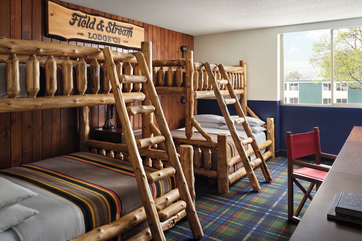 Ett rum inrett i rustik stil med våningssängar, en rutig matta och en träskylt med texten ”Field & Stream Lodge Co.”.