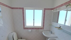 A bathroom with a toilet, bidet, two sinks, and a window. - Carpe Diem (faro)