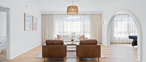 Een ruime woonkamer met een houten vloer, twee bruine banken, een salontafel en een hanglamp.