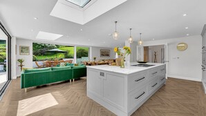 Een moderne keuken met een groot eiland, een eethoek met groene banken en uitzicht op een tuin door grote ramen.