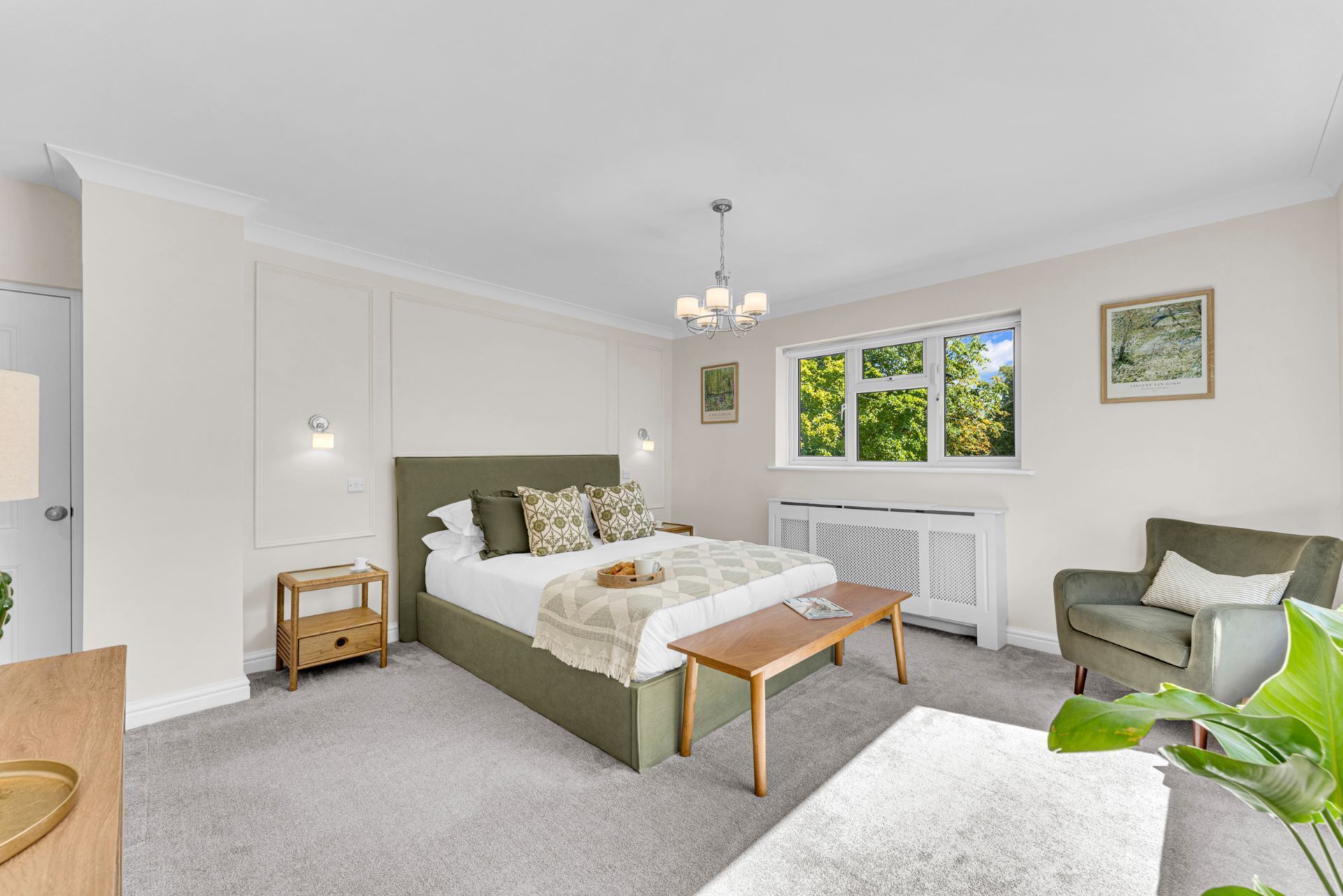 A bedroom with a bed, bedside table, chair, and a window with a view of trees.