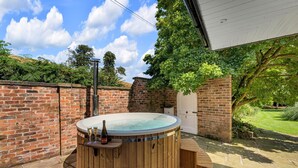 Een hottub met een houten buitenkant, een bakstenen muur en een deur, gelegen in een tuin.