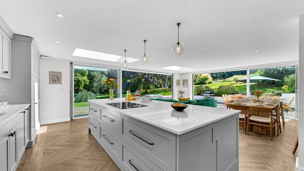 Een moderne keuken met een groot eiland, witte kasten en uitzicht op een weelderige tuin door grote ramen.