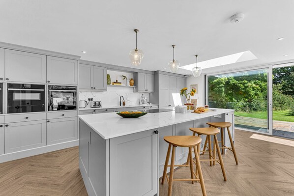Cocina moderna con una isla grande, taburetes de madera y vistas a un jardín a través de un ventanal corredero.
