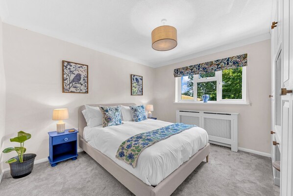 Un dormitorio con cama, mesitas de noche, ventana con cortinas y decoración en la pared.