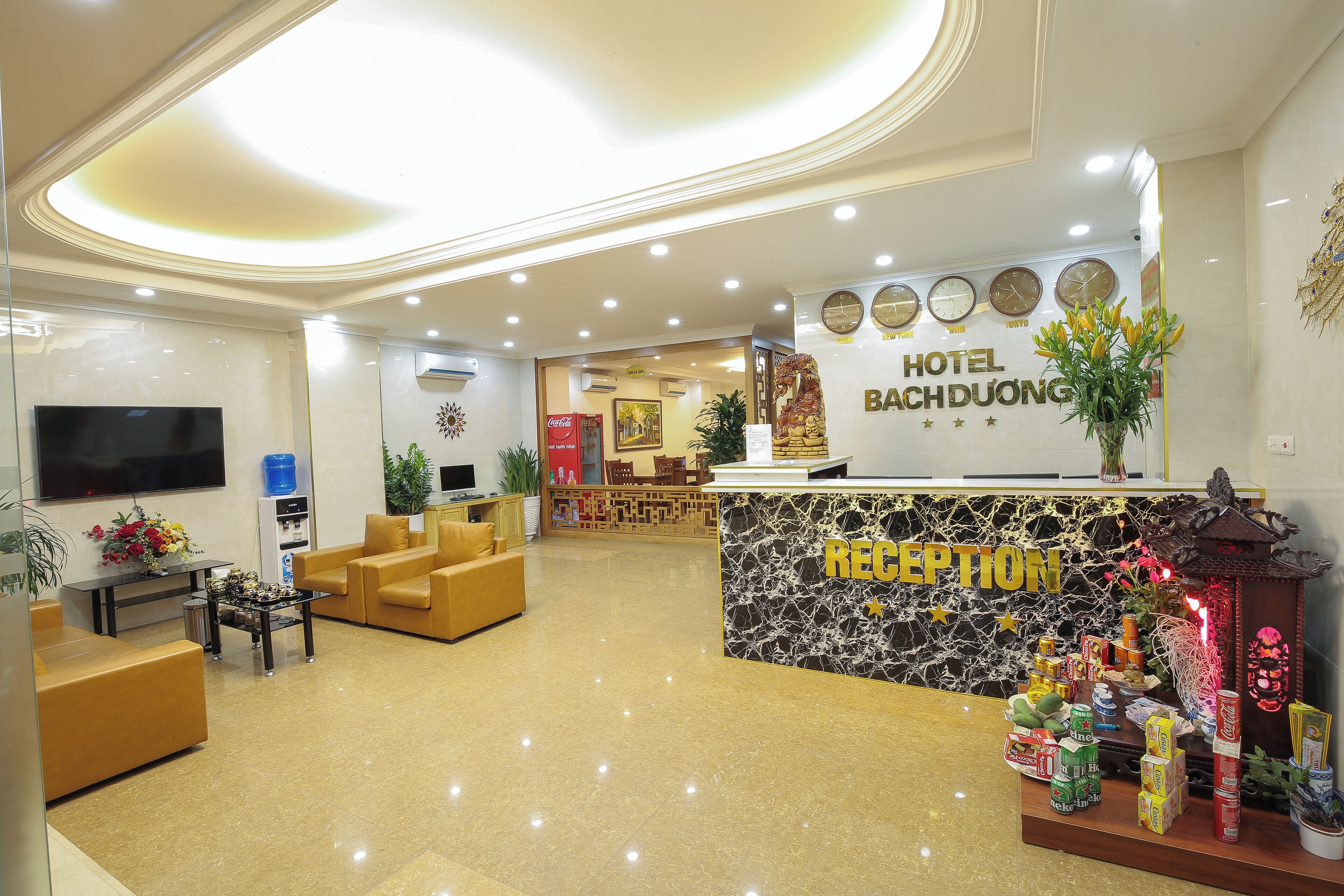 A hotel reception area with a marble counter, sofas, a TV, and a decorative reception desk.