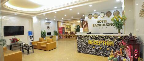 A hotel reception area with a marble counter, sofas, a TV, and a decorative reception desk.