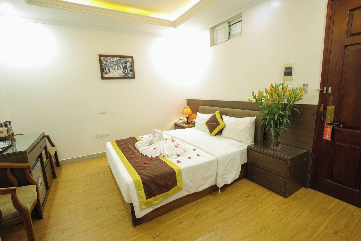 A hotel room with a bed, bedside table, lamp, and a vase with flowers.