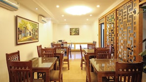 Un área de comedor con mesas y sillas de madera, un separador de vidrio y dos cuadros en las paredes.