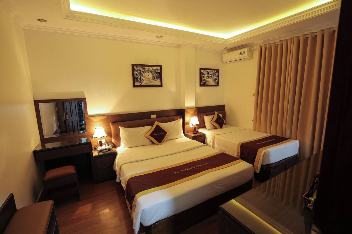 A hotel room with two beds, a desk, a chair, a mirror, and a nightstand with a lamp.